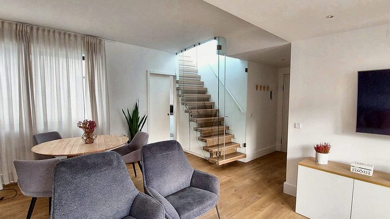 Round dining table with armchairs and the floating wooden staircase behind glass