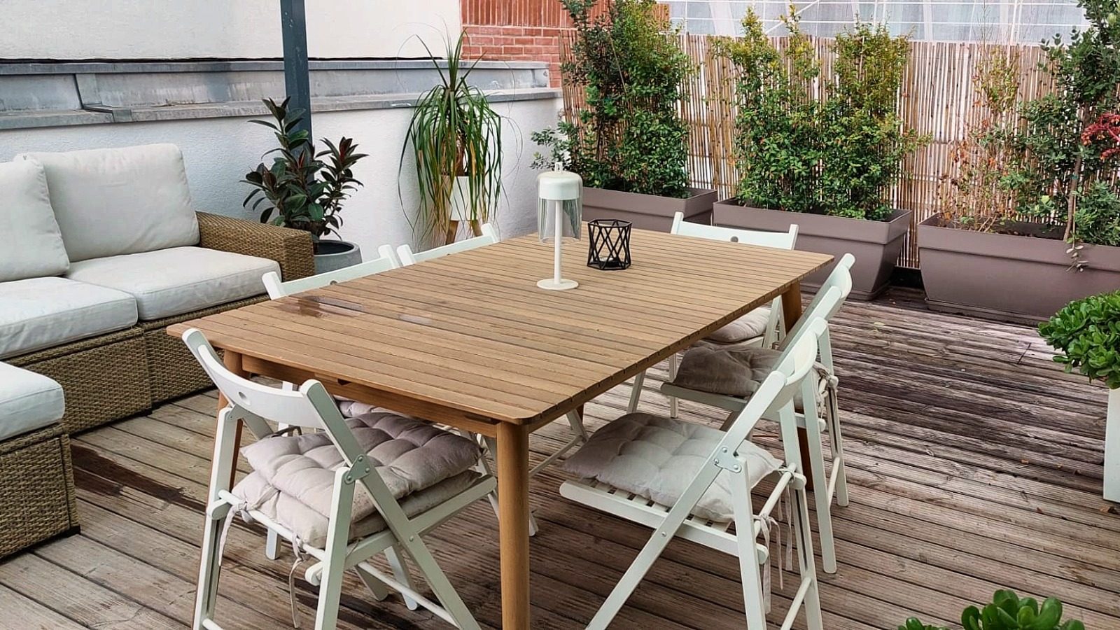 Dining table and outdoor sofas on the wooden deck of the upper terrace, with planters along the railing